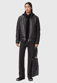 Sort læderjakke med lynlås, sort h�ættetrøje under, mørk denim bukser, sorte sko, holder en struktureret sort totebag.