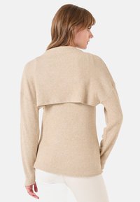 Maglione beige a coste con maniche lunghe e design a strati sul retro. Tessuto morbido e vestibilità rilassata, adatto per abbigliamento casual.