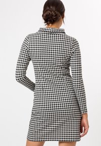 Robe à motif pied-de-poule noir et blanc avec manches longues et col, présentant une silhouette ajustée et une texture de tissu lisse.