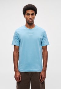 Hele sinine puuvillane t-särk ümara kaelusega, lühikeste varrukatega ja väikese valge logoprindiga rinnal keskel. Sile tekstuur.