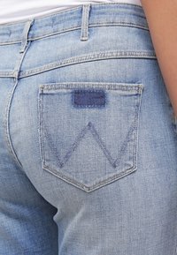 Vaaleansinisiä farkkuja, joissa on takatasku, jossa on tumman sininen zick-zack-kuvio, hienovaraisia ompeluyksityiskohtia ja normaali vyötärö.