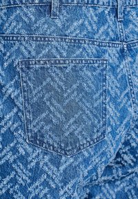 Blue denim jeans feature a textured zigzag pattern, a rear pocket, and classic stitching details, highlighting its distinct design.