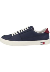Zapatilla de cuero azul marino con cordones blancos, suela de goma, acento rojo en el talón y logo de Tommy Jeans en el lateral. Textura suave, diseño bajo.