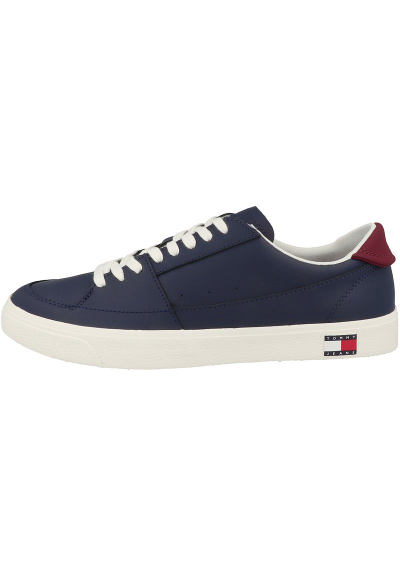 Zapatilla de cuero azul marino con cordones blancos, suela de goma, acento rojo en el talón y logo de Tommy Jeans en el lateral. Textura suave, diseño bajo.