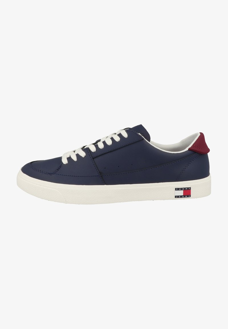 Zapatilla de cuero azul marino con cordones blancos, suela de goma, acento rojo en el talón y logo de Tommy Jeans en el lateral. Textura suave, diseño bajo.