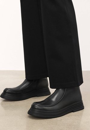 Black leather ankle boots with a raised, textured sole and smooth finish. Sleek design with minimalist details and elastic side panels.
