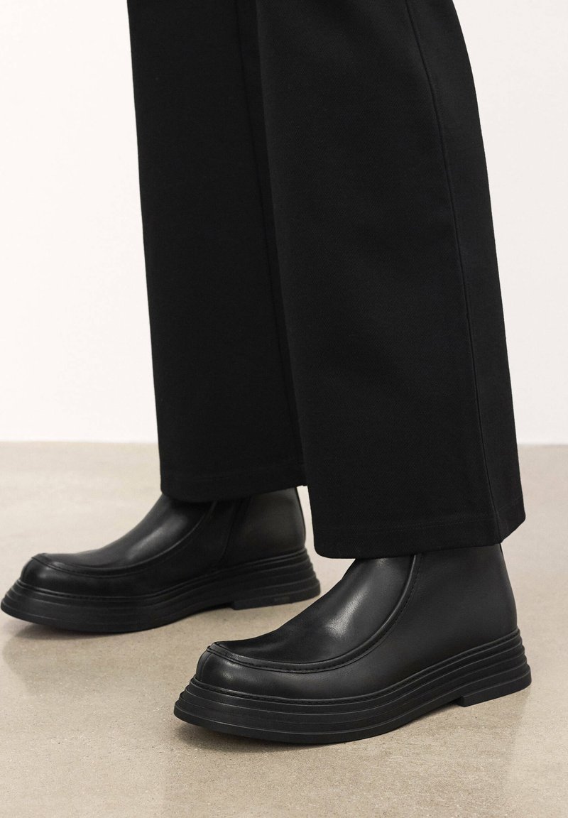 Botine negre din piele, cu o talpă texturată ridicată și un finisaj neted. Design elegant cu detalii minimaliste și panouri laterale elastice.