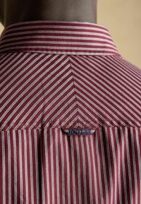 Rød- og hvidstribet skjorte med kridhvid krave, der har et lille blåt mærke med ordet "JOUERT" på bagstykket.