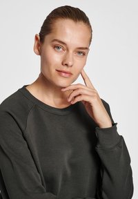 Mörkgrön sweatshirt med rundad halsringning och ribbad mudd, med en slät textur och minimalistisk design.