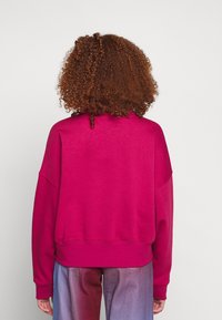 Fuksjowa, oversize'owa bluza z okrągłym dekoltem, ściągaczem u dołu i opadającymi ramionami, w połączeniu z spodniami w gradientowych kolorach.