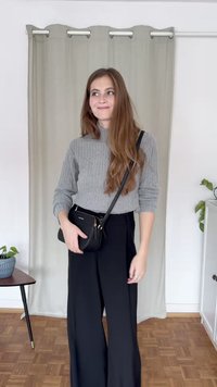 Un maglione grigio a collo alto a coste abbinato a pantaloni neri a gamba larga. Una piccola borsa a tracolla nera con zip completa il look.