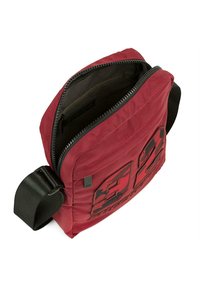 Bolso de hombro de tela roja con apertura con cremallera, diseño acolchado y correa negra. Presenta un logotipo y acentos texturizados en la parte frontal.