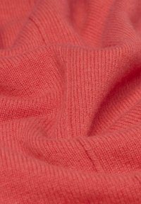 Tissu en tricot corail avec une texture douce, présentant un détail côtelé. Le matériau semble chaud et confortable, mettant en avant des fibres lisses et entrelacées.