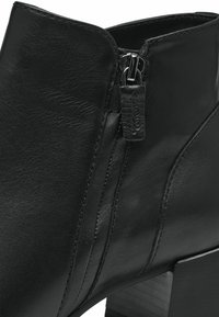 Stivale alla caviglia in pelle nera con zip laterale e tacco spesso. Finitura texturizzata con dettagli di cucitura lungo le cuciture.