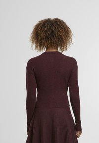 Pull en maille bordeaux avec une coupe ajustée. Manches longues, texture côtelée aux poignets et à l'ourlet. Encolure ronde simple, sans motifs ni accents visibles.