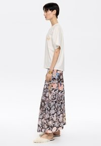 Camiseta de algodón color crema con mangas cortas y texto bordado, combinada con una falda larga floral en gris, rosa y azul, utilizada con suaves pantuflas.