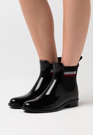 Bottines en caoutchouc noires avec une finition brillante, panneaux latéraux élastiques à motif zigzag rouge et blanc, et un petit talon.