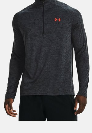 Mørkegrå langærmet atletisk top med halv lynlås, subtil tekstur og en kontrastfuld orange logo på brystet. Har opretstående krave og tætsiddende ærmer.