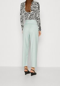 Zebra-print langemouwen top gecombineerd met lichtblauwe hoge taille wijde pijpen broek. Zwarte wedgesandalen maken de outfit af.