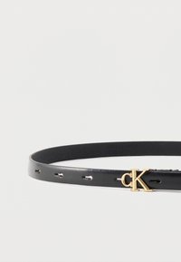 Μαύρη δερμάτινη ζώνη με αγκράφα λογότυπου "cK" σε χρυσό και πολλαπλές τρύπες ρύθμισης, σε απλό λευκό φόντο.