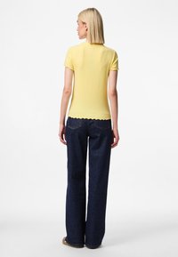 Dzeltena ribotā īsām piedurknēm tops ar viļņotām malām, apvienots ar augsta vidukļa tumši ziliem platām biksēm, uzsverot brīvāko piegriezumu.