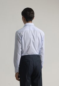 Camisa abotonada a cuadros azul claro con mangas largas, combinada con pantalones oscuros de corte ajustado. Presenta un cuello estándar y puños de doble botón.
