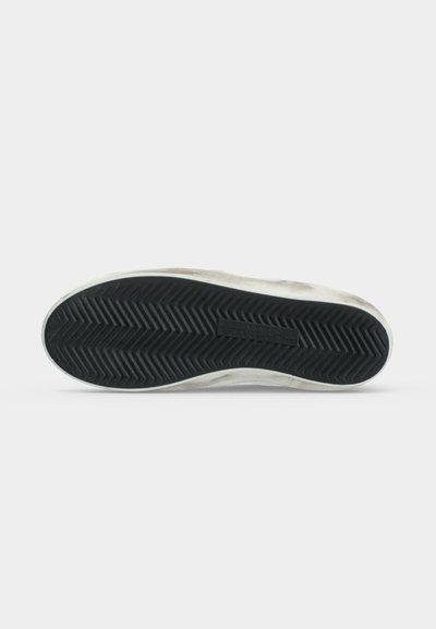 Semelle de basket en caoutchouc noir avec motif en chevrons, vue de dessous sur fond blanc uni. Aucune personne ou objet supplémentaire visible.