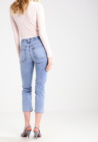 Světle modré džíny s vysokým pasem, vystřihnutým střihem, roztrhaným lemem a charakteristickým designem zadní kapsy. V kombinaci se šedými lodičkami na podpatku.