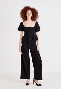 Top peplum nero in tessuto testurizzato, scollatura quadrata e maniche a sbuffo, abbinato a jeans neri a vita alta e a gamba larga e tacchi a punta neri.