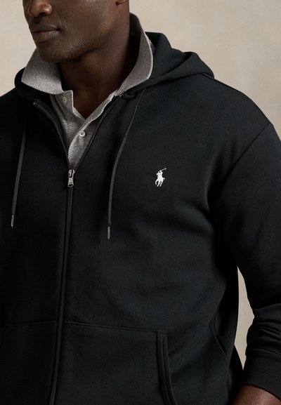 Svart zip-up hoodie i mjukt tyg med en huva fodrad i grått, med en vit polo-logga på bröstet och framfickor.