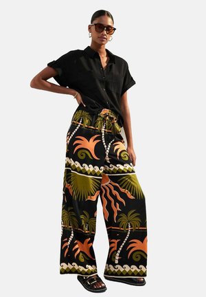 Camicia nera a maniche corte abbinata a pantaloni larghi con un vivace motivo di palme e sole in arancione e verde su sfondo nero.