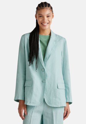 Blazer en lin bleu clair avec deux boutons, revers crantés et poches latérales, associé à un top vert. Texture lisse, coupe décontractée.
