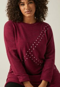 Felpa bordeaux con maniche lunghe, caratterizzata da una linea diagonale di paillettes argento. Texture morbida e vestibilità rilassata.