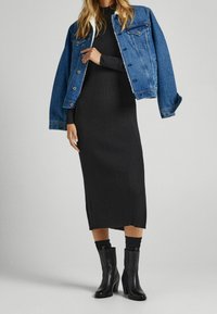 Džínsová bunda s kožešinovým límcem, nošená přes černou kostýmovou midi šaty. Černé vysoké boty až po kolena s texturovaným povrchem.