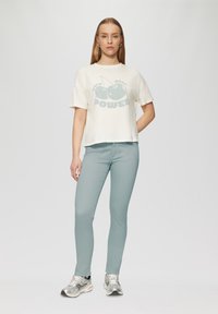 Lichtcrème, kort T-shirt met een kersengrafiek en de tekst "POWER". Een paar lichtblauwe, aansluitende broeken. Zilveren sportschoenen. Eenvoudige achtergrond.