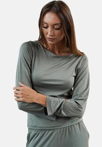 Długi rękaw, bluzka z miękkiego, jasnego zielonego materiału o luźnym kroju. Posiada zaokrąglony dekolt i zaokrąglone mankiety. Gładka faktura, minimalistyczny design.