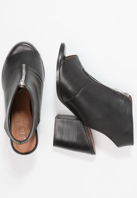 Czarne skórzane botki z odkrytymi palcami i srebrnym zamkiem z przodu, z blokowym obcasem, przedstawione z widoków z góry i z boku na białym tle.