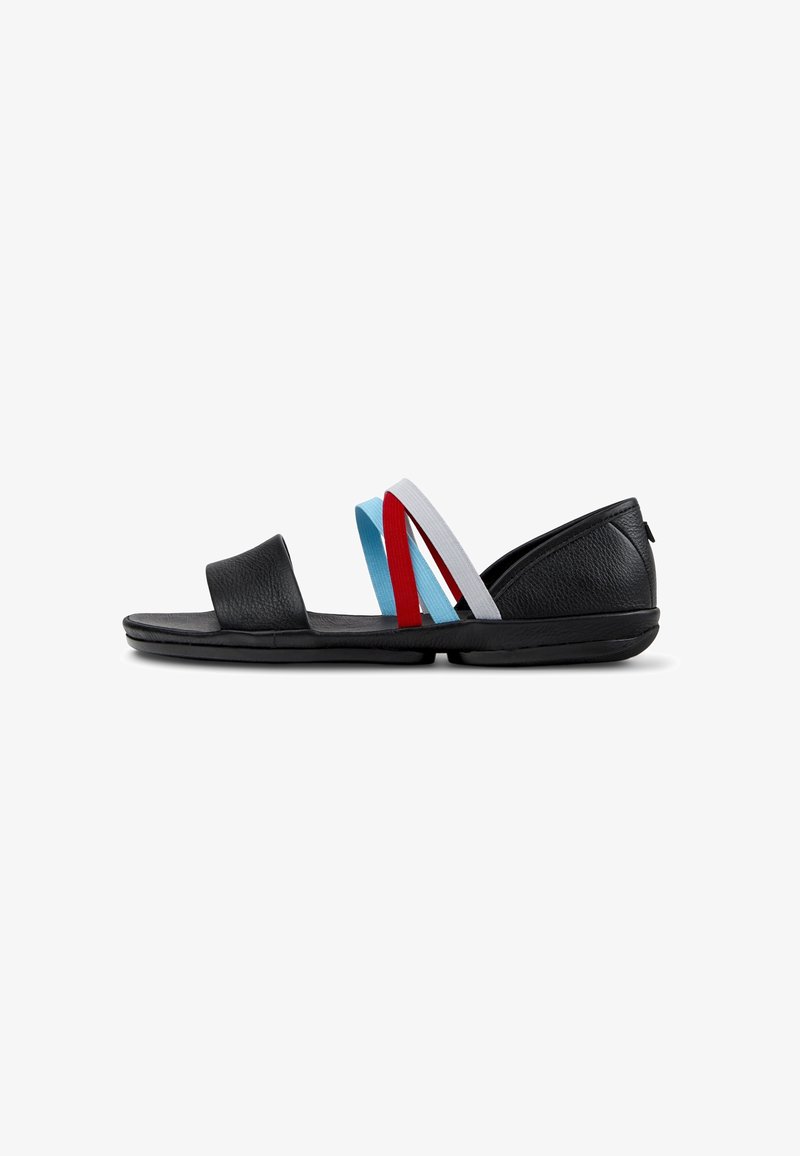 Sandale plate noire avec bout ouvert, talon arrière, et trois lanières élastiques en bleu clair, rouge et blanc traversant le cou-de-pied.