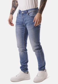 Jeans in denim azzurro chiaro con una vestibilità slim, design a cinque tasche e cuciture a contrasto, abbinati a sneakers bianche.