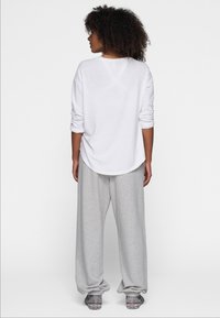 Camicia bianca a maniche lunghe con scollatura tonda, abbinata a pantaloni felpati grigi chiari e larghi. Tessuto testurizzato, design minimale.