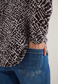 Bluse med sort-hvidt mønster og lange ærmer, nedstoppet i blå denim jeans. Stoffet har en blød tekstur; jeansene har klassisk fem-lomme stil.