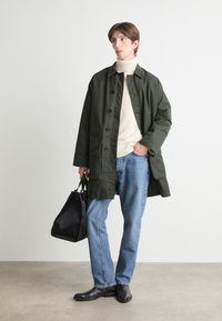 Olivengrøn vandafvisende frakke, cremefarvet turtleneck sweater, blå jeans, sorte læderstøvler og en sort struktureret taske. Glatte teksturer, afslappet pasform.