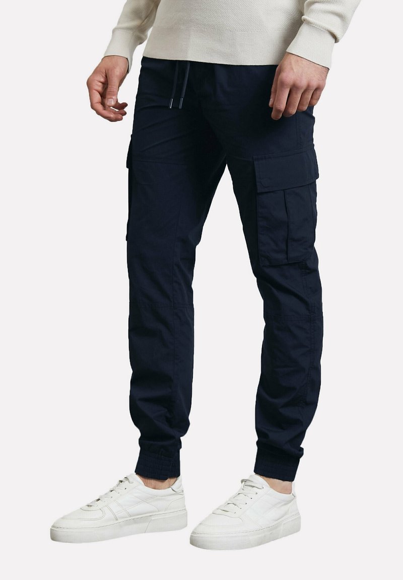 Pantalon cargo bleu marine avec plusieurs poches cargo, poignets élastiques et taille à cordon, fabriqué en tissu durable, assorti à des baskets blanches.