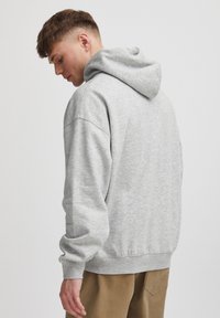 Haut à capuche en coton gris avec une coupe décontractée, des poignets et un ourlet côtelés. Il dispose d'une capuche à cordon de serrage et d'un design d'épaule sans couture.