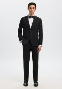 Czarny garnitur smokingowy z jednorzędową marynarką, białą koszulą i muszką. Dopasowany krój, gładka tkanina i minimalistyczny design.