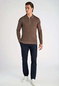 Brun långärmad polo t-shirt med dragkedja i kragen, kombinerad med mörkblå byxor och vita sneakers. Slät stickad textur; åtsittande design.