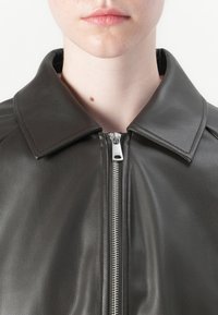Svart skinnjakke med stor krage, frontglidelås og synlige sømdetaljer. Glatt tekstur og tettsittende design.