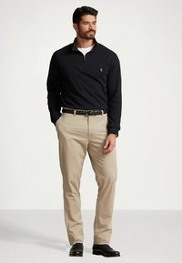 Mörkblå pullover med dragkedja vid halsen och logga, khakifärgade chinos, vävd svart bälte och svarta skor. Enkel design med kontrasterande material och färger.