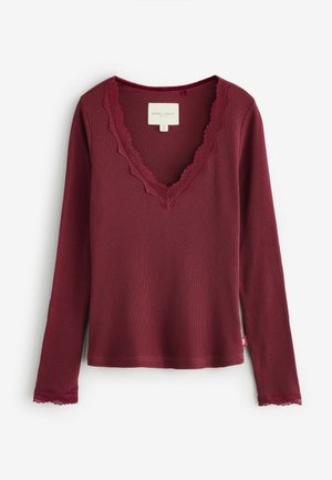 Burgundy pitkähihainen paita, jossa on ribbikuvio ja pitsireunainen V-kaula-aukko. Pitsi korostaa hihansuiden reunaa, ja tagi on näkyvissä sivulla.
