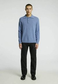 Mėlynas megztinis su apykakle ir trimis mygtukais, derinamas su juodomis kelnėmis ir juodais batais. Lygaus paviršiaus, laisvalaikio dizainas.